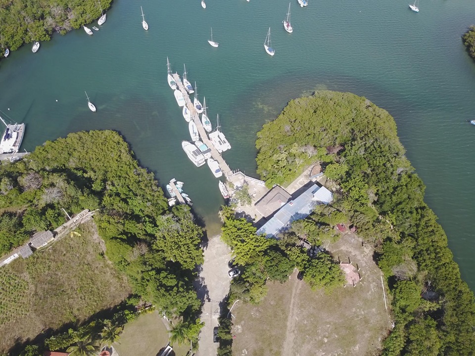 looking down on a long pontoon with boats tied to it and boats anchored just off the pontoon surrounded by mangroves