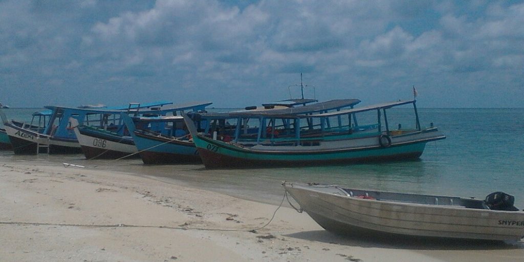 a small cruising yacht dinghy pulled up on a white sandy beach next to a line of local work boats