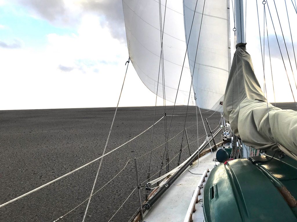 Sailing yacht surrounding by grey pumice on the ocean.