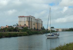 a waterway canal with green grass either side and a tall apartment building with a boat motoring along the canal