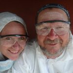 couple dressed in white overhauls and clear goggles, dressed to paint the keel of their boat