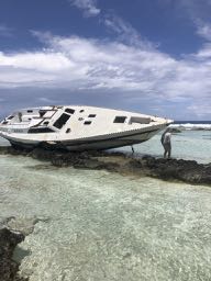 a yacht lying on its side dry on the reef stripped bare with no mast