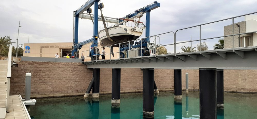 from water level looking up at a travelift with a boat suspended in its slings