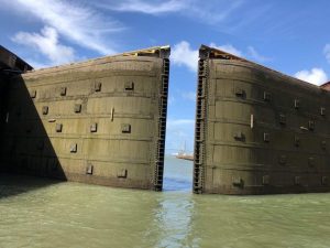 big lock doors dark grey with water half way up them almost closed with just a view of the sea behind