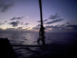 twilight at sea with an almost purple sky and small white moon rising