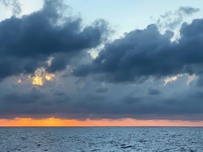 close up of the intense pink of a sunrise and building clouds in a line above it